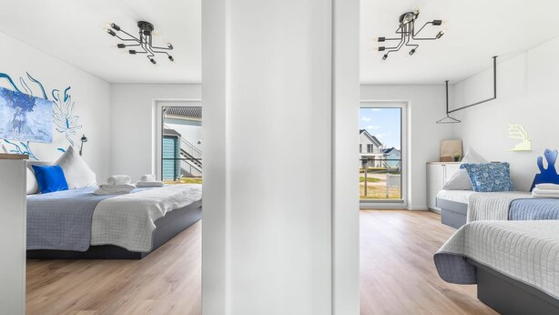 A modern hotel room with a large window, a bed with a grey and white duvet, a blue pillow, and a wall-mounted light fixture. - Pet friendly apartment in Olpenitz (Olpenitz)