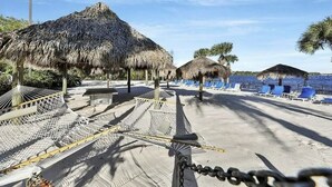 A beach with thatched-roof structures, a sandy area, and blue lounge chairs. - Bahama Bay Resort * Disney Area * Free Parking (Davenport)