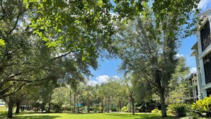 A well-maintained grassy area with mature trees and a building with multiple windows and balconies. - Bahama Bay Resort * Disney Area * Free Parking (Davenport)