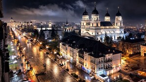 A nighttime cityscape with a prominent church featuring three domes and a large building with a clock tower. - Exodus - Iasi City Center (Iași)