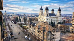 A historic building with three domes, a central tower, and a large open square with pedestrians and vehicles. - Exodus - Iasi City Center (Iași)