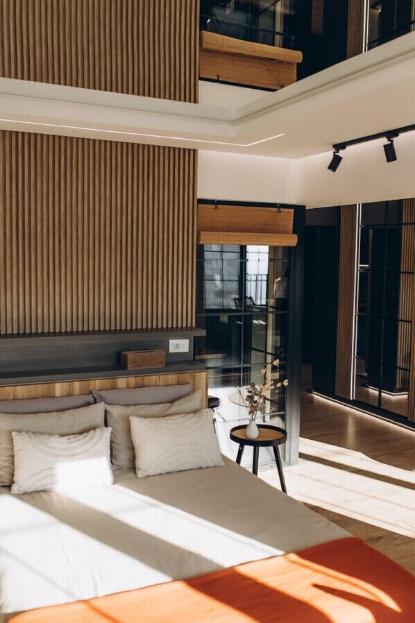 A modern bedroom with a large bed, a wooden slatted wall, and a glass door leading to a balcony.