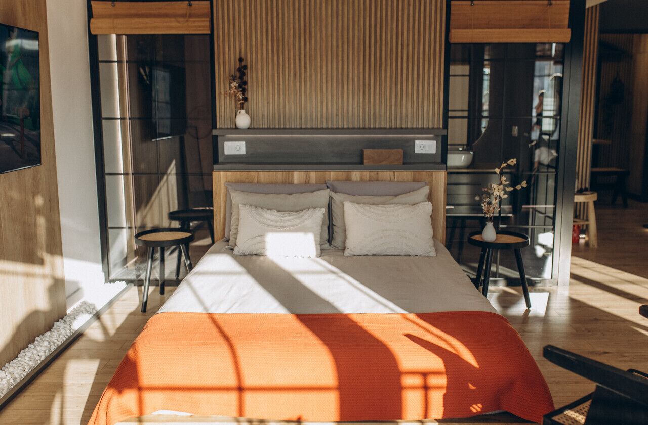 A modern bedroom with a large bed, a wooden headboard, and a small table with a vase.