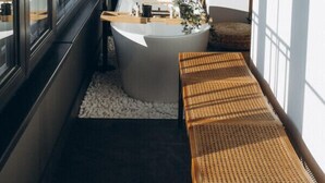 Ein modernes Badezimmer mit einer freistehenden Badewanne, einer Holzbank und großen Fenstern mit Blick auf die Stadt.