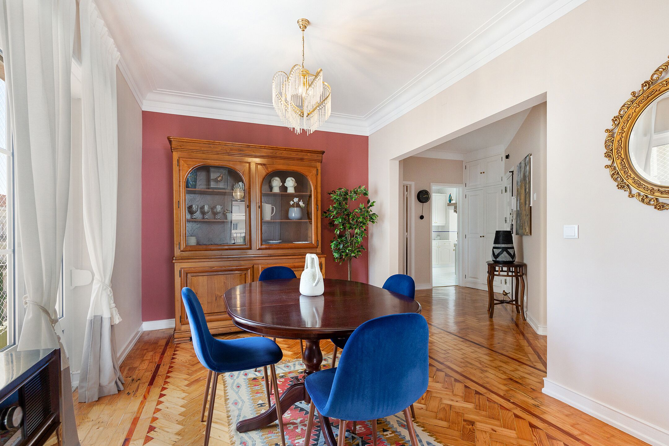 A dining room with a wooden dining table, blue chairs, a chandelier, and a large wooden cabinet with glass doors.
