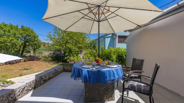An outdoor patio with a table set for breakfast, a large umbrella, and a chair. - Pool House Franjo (Dobrinj)