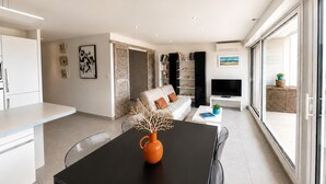 A modern living room with a sofa, TV, and dining area. - Rose des Sables • A Terrace Over the Mediterranean (Mauguio)