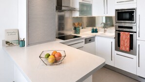 A modern kitchen with white cabinets, stainless steel appliances, a glass bowl with fruit, and a book on the counter. - Rose des Sables • A Terrace Over the Mediterranean (Mauguio)