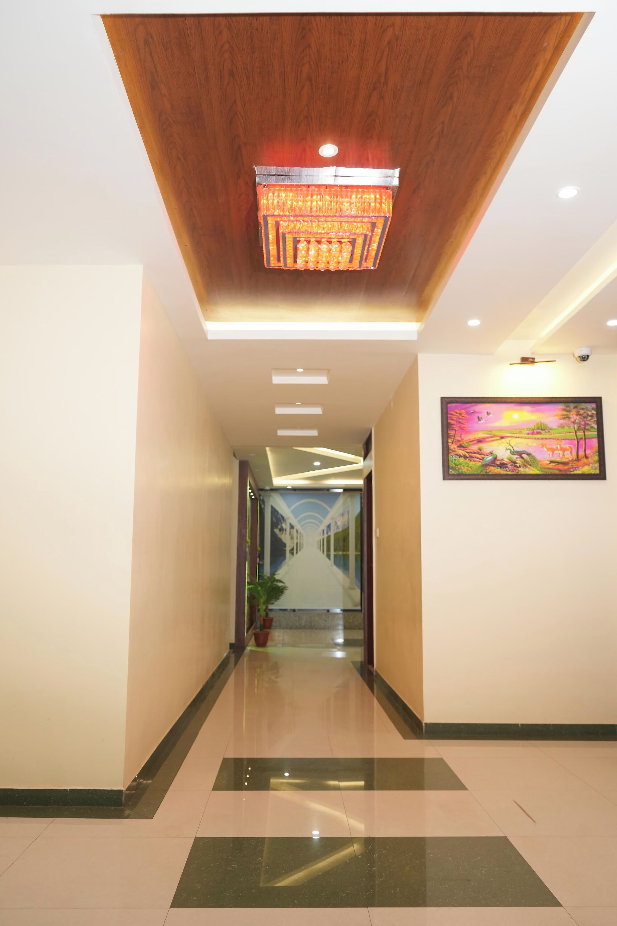 A hallway with a wooden ceiling, a chandelier, recessed lighting, a potted plant, and a painting on the wall.