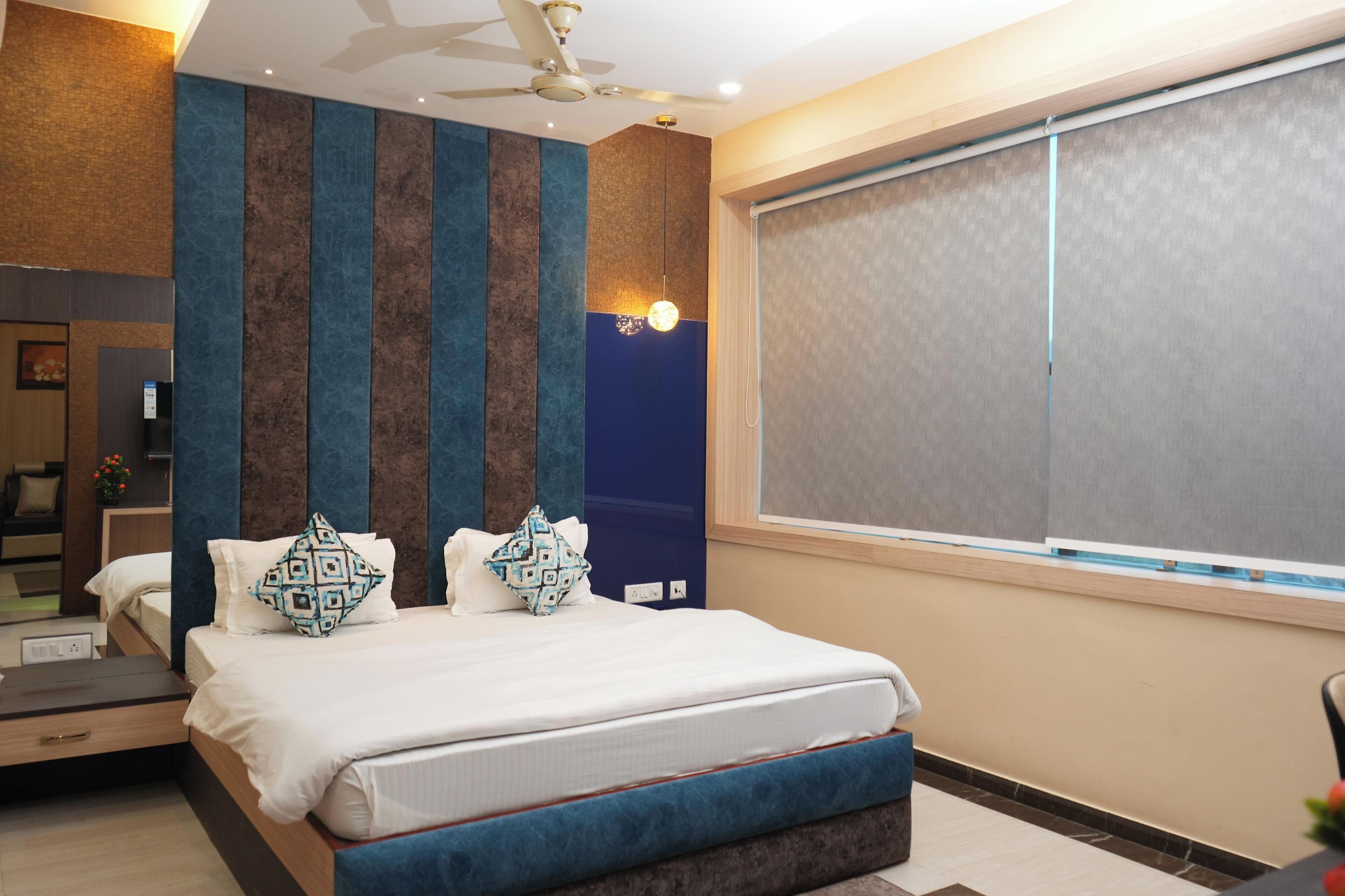 Ein modernes Hotelzimmer mit einem großen Bett, einem Deckenventilator und einem großen Fenster mit Jalousien.