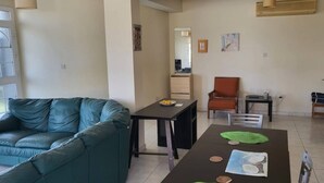 Una sala moderna con un sofá verde, una mesa de comedor con individuales verdes, y una zona de cocina al fondo.