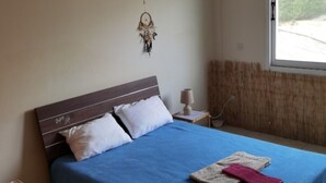 Un dormitorio con cama, mesita de noche, lámpara, atrapasueños y ventana con vistas a la vegetación.