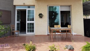 Un edificio residencial con un patio que tiene una mesa, sillas, una puerta corrediza de vidrio y plantas en macetas.