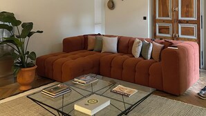 A living room with a sectional sofa, a glass coffee table, a potted plant, and a door with decorative panels. - Le Jardin des Etudes - Terrace & Mansion 300 Years (Avignon)