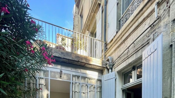 A courtyard with a round table, potted plants, and a building with grey shutters. - Le Jardin des Etudes - Terrace & Mansion 300 Years (Avignon)