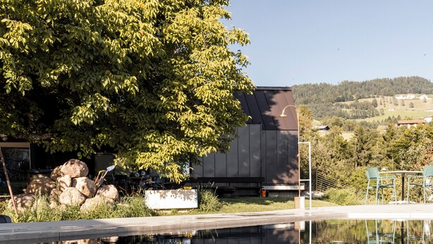 A modern building with a reflection in a calm water body, surrounded by greenery and a clear sky. - Michlhaus nature and suites (Aldino)