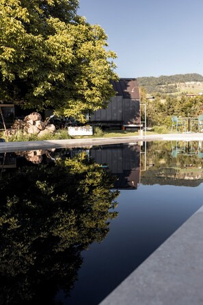 A modern building with a reflection in a calm water body, surrounded by greenery and a clear sky. - Michlhaus nature and suites (Aldino)