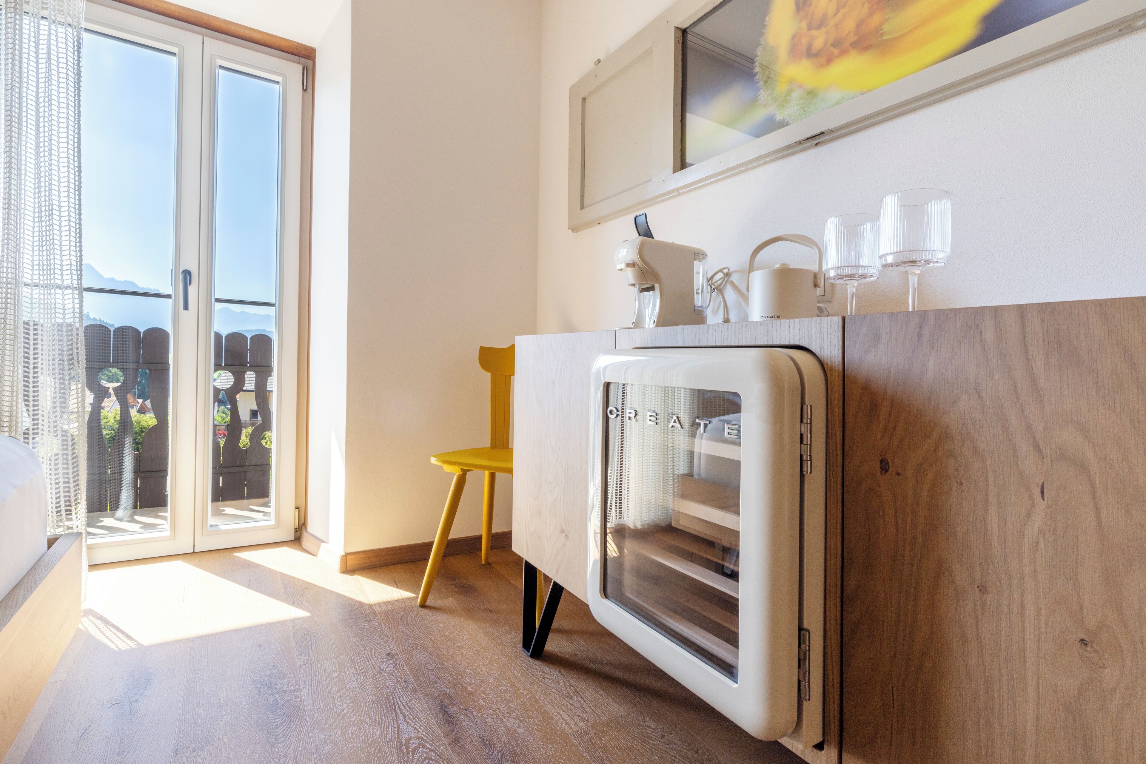A modern room with a sliding glass door leading to a balcony, a wooden cabinet with a mirror, and a small yellow chair.