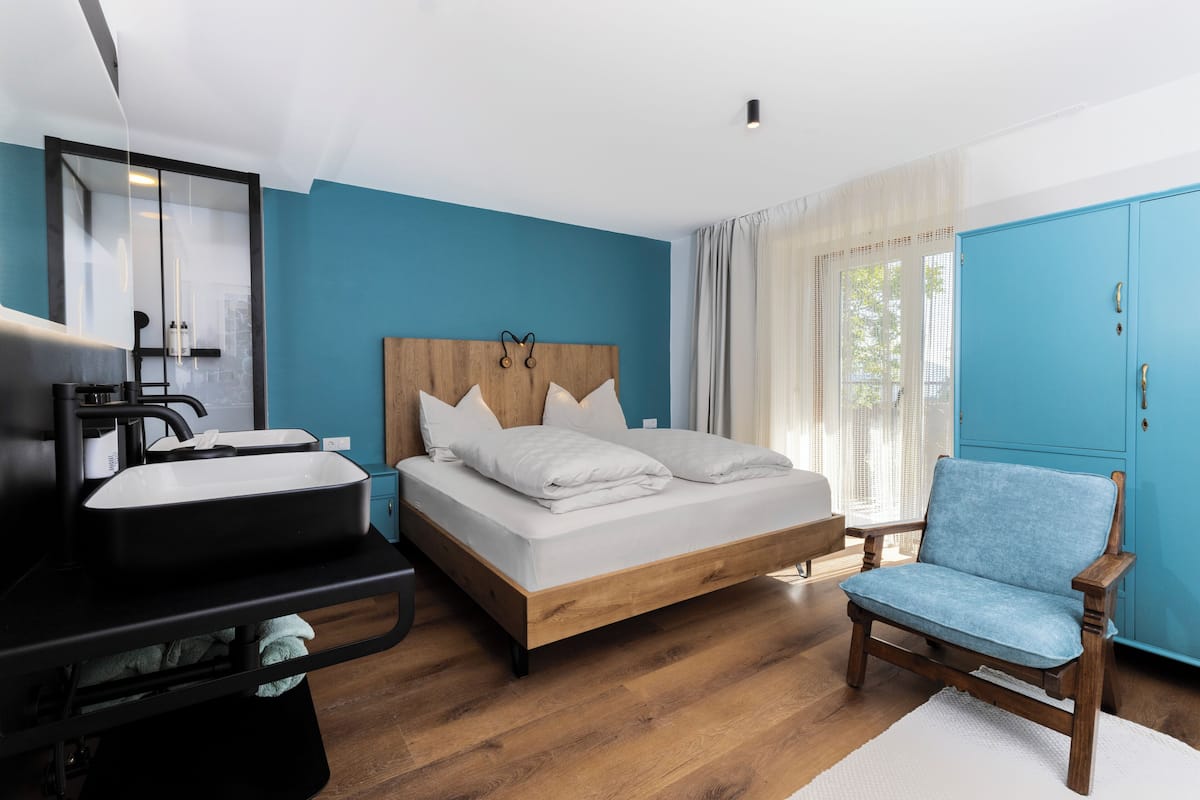 A bedroom with a bed, a chair, a sink, and a wardrobe.