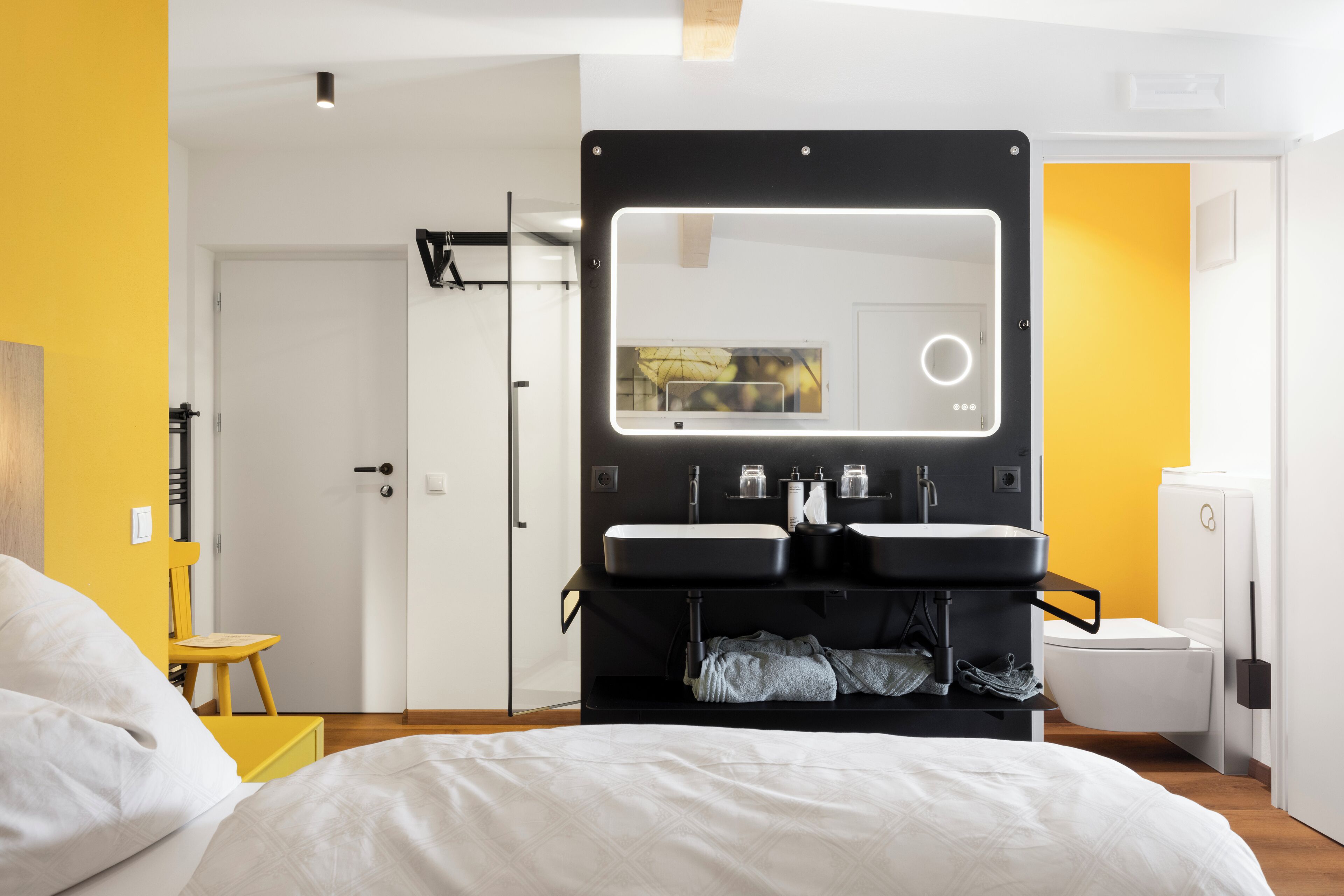 Et moderne hotelværelse med seng, stort spejl, to håndvaske og toilet.
