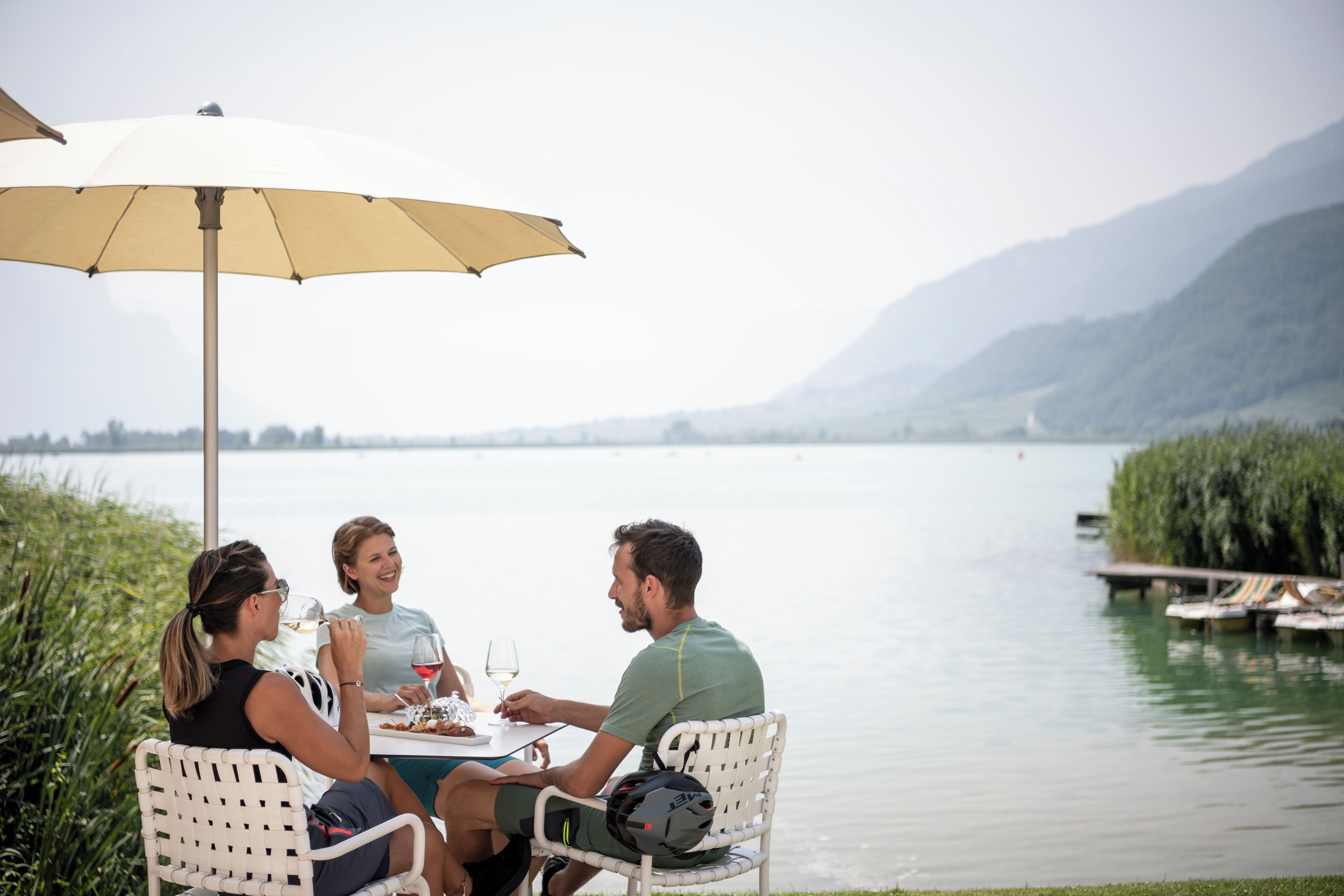 Three people dining at a table with a view of a lake and mountains in the background.