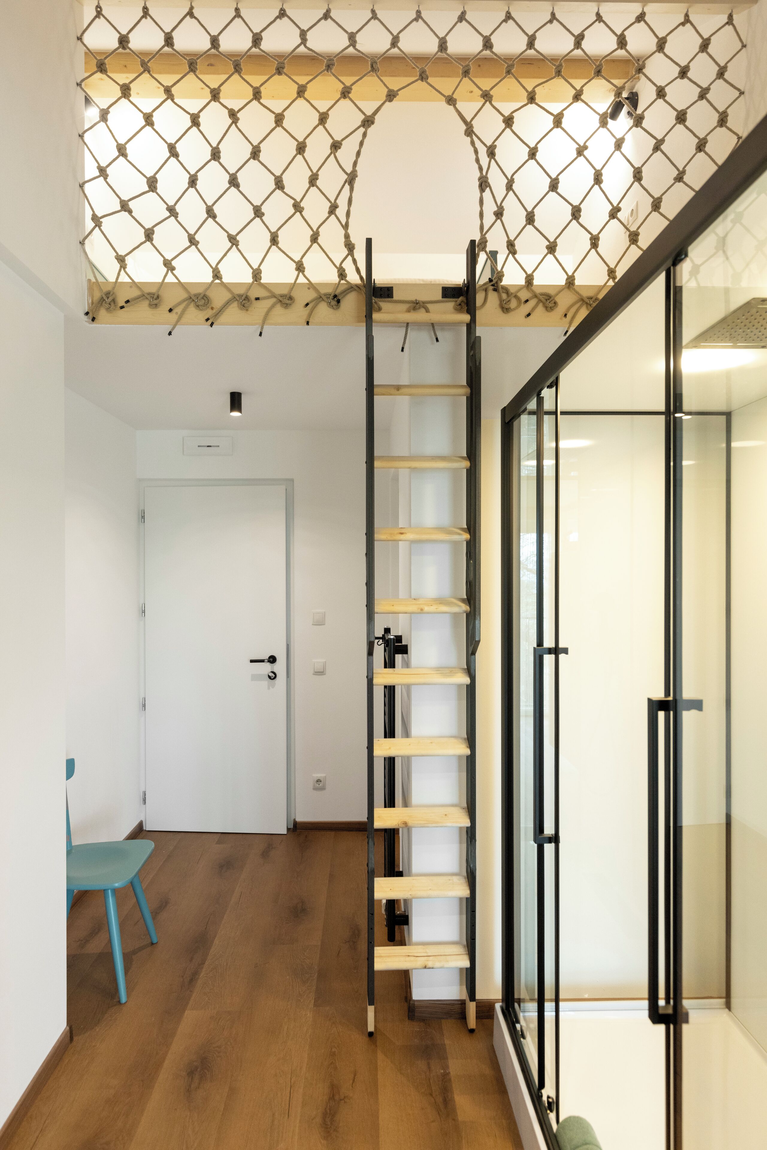 A room with a wooden ladder, a blue chair, and a glass door.