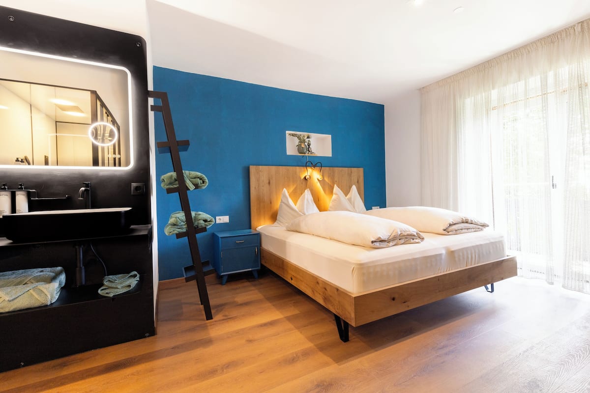 A bedroom with a bed, bedside table, and a mirror with lights.
