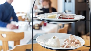 A three-tiered serving tray with various food items, including a white dessert and some meat, in a dining setting. - Michlhaus nature and suites (Aldino)