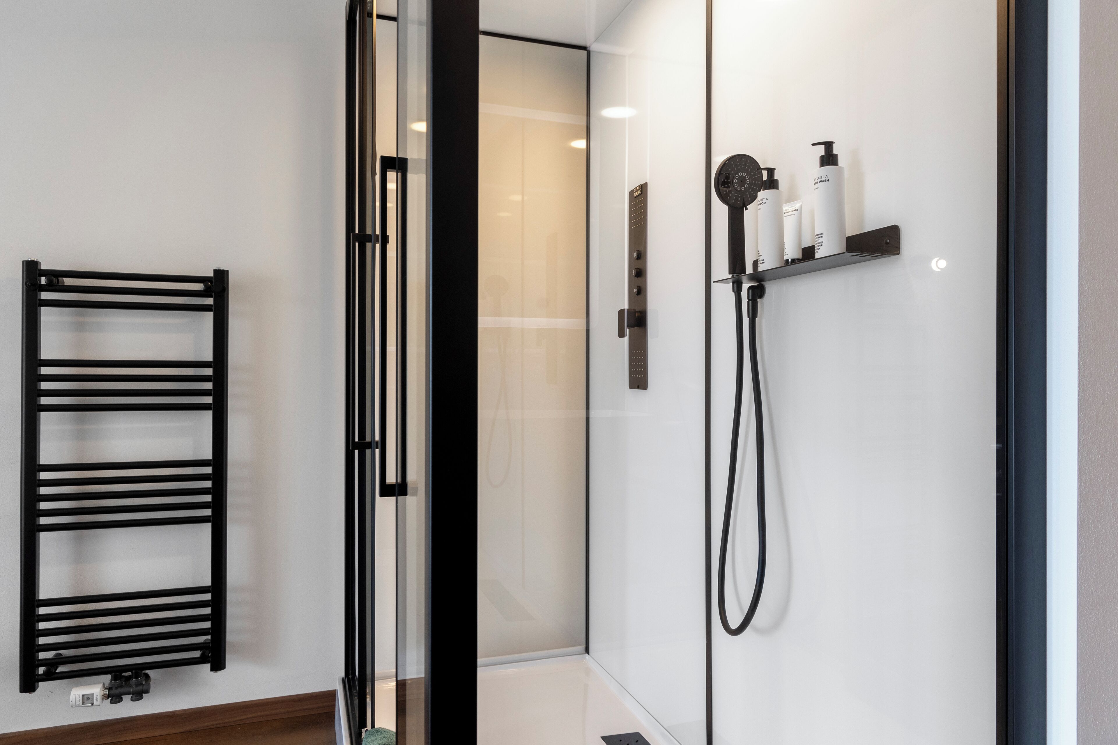 Un baño moderno con cabina de ducha de vidrio, un perchero negro y un estante con artículos de tocador.