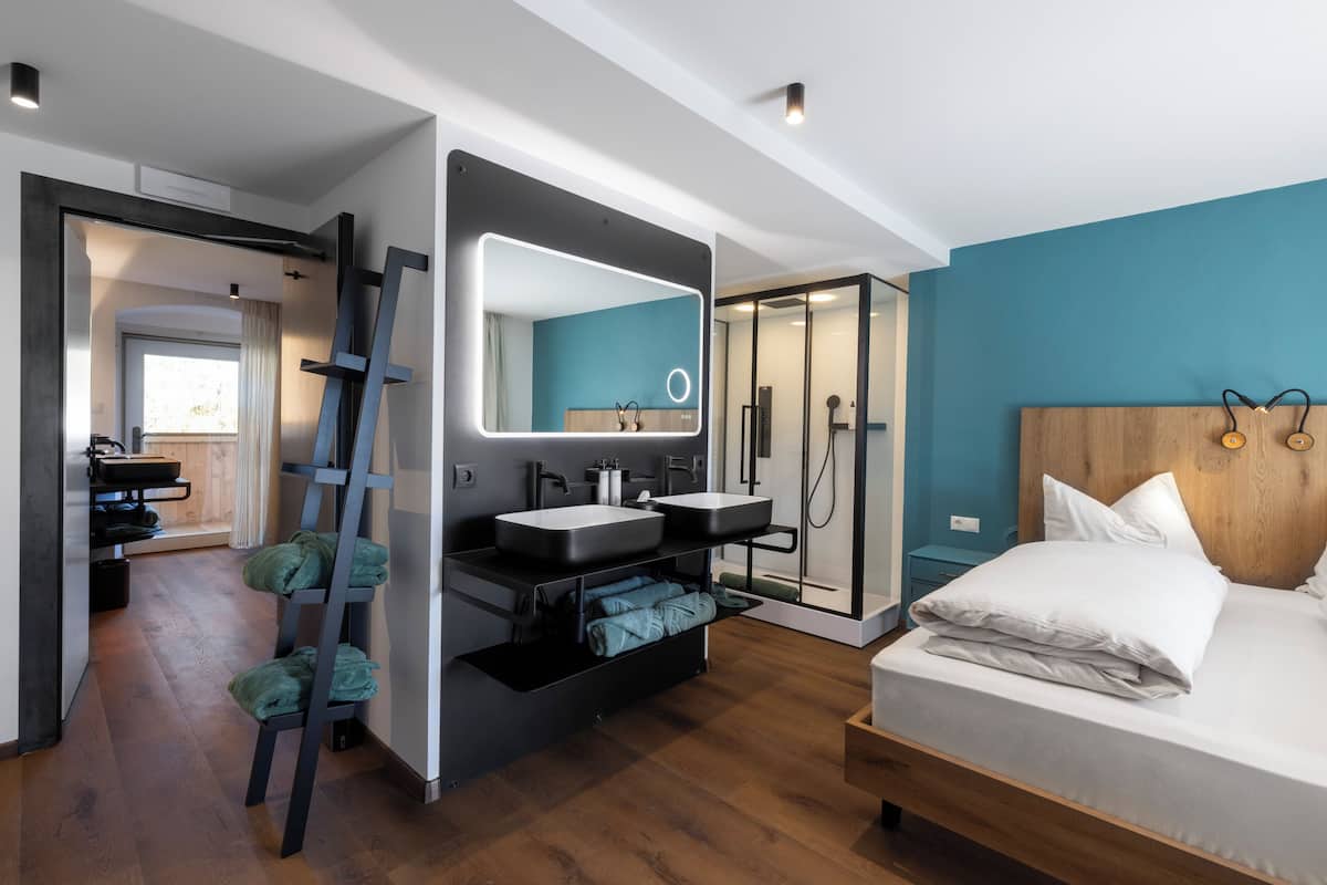 A modern bedroom with a large bed, a built-in vanity with dual sinks, a shower, and a ladder against the wall.