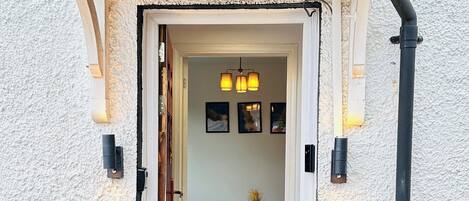 A doorway leading into a room with a table and chairs, a hanging light fixture, and a wall-mounted light.