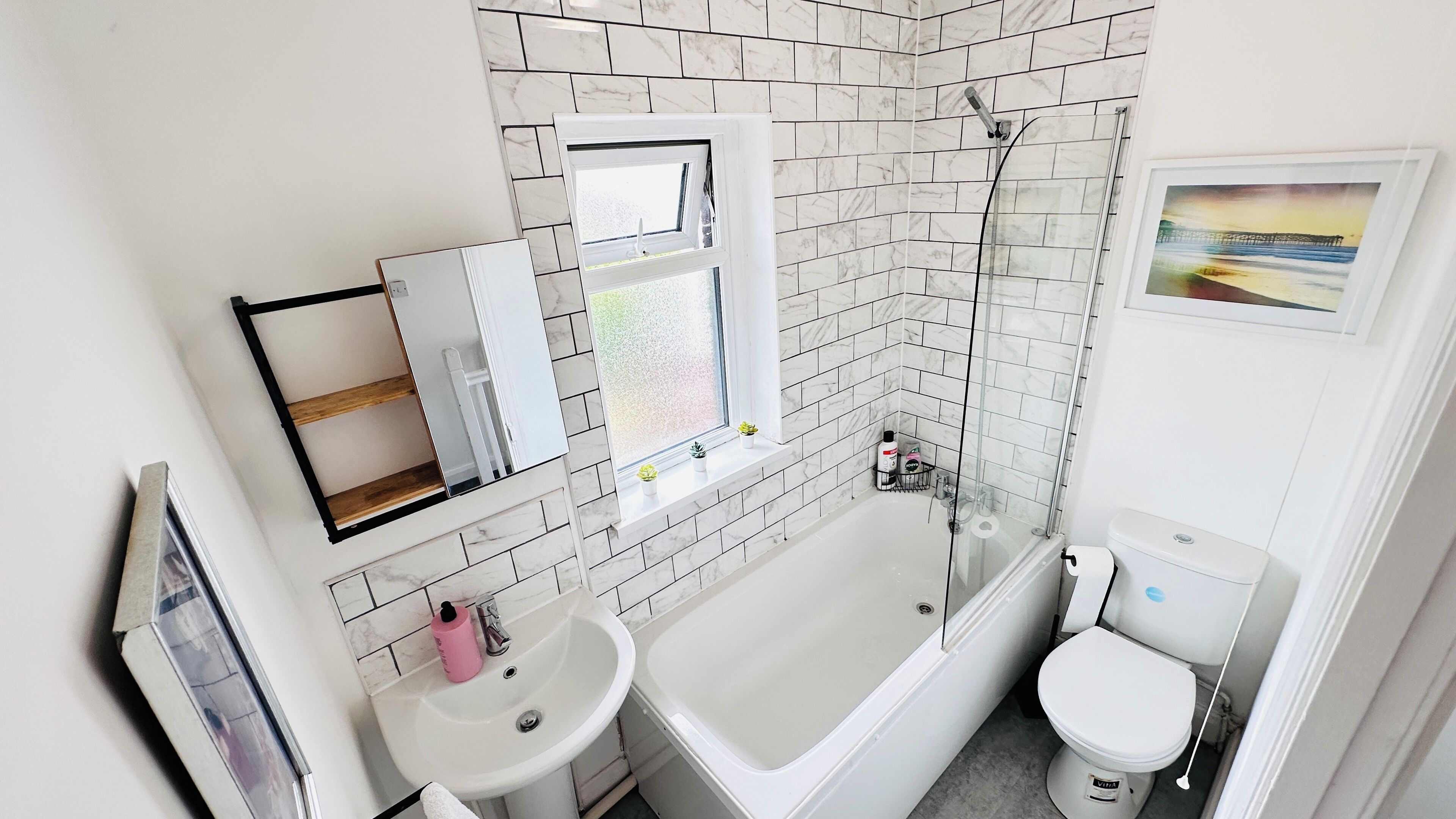 A bathroom with a bathtub, toilet, sink, and a window with a view of the sea.