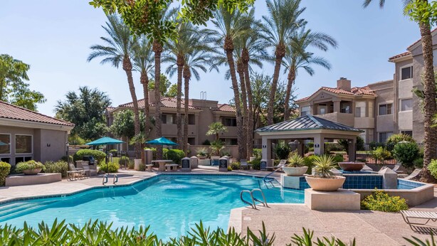 A swimming pool surrounded by palm trees and lounge chairs, with a building in the background. - Modern Retreat in Ahwatukee, Heated Pool, Spa, Gym (Phoenix)