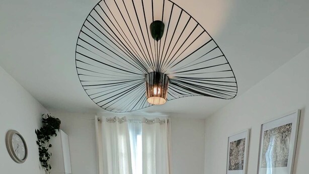 A modern living room with a sectional sofa, a dining table with a plastic cover, a TV on a stand, and a unique ceiling light fixture. - Quiet house between Disneyland and Paris (Villiers-sur-Marne)