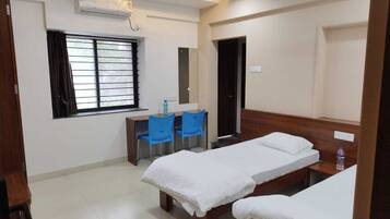 A hotel room with two beds, a desk, two chairs, a window with curtains, an air conditioner, and a ceiling fan.
