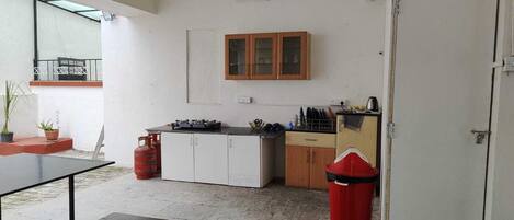 A compact kitchen with a gas stove, wooden cabinets, and a red trash bin.