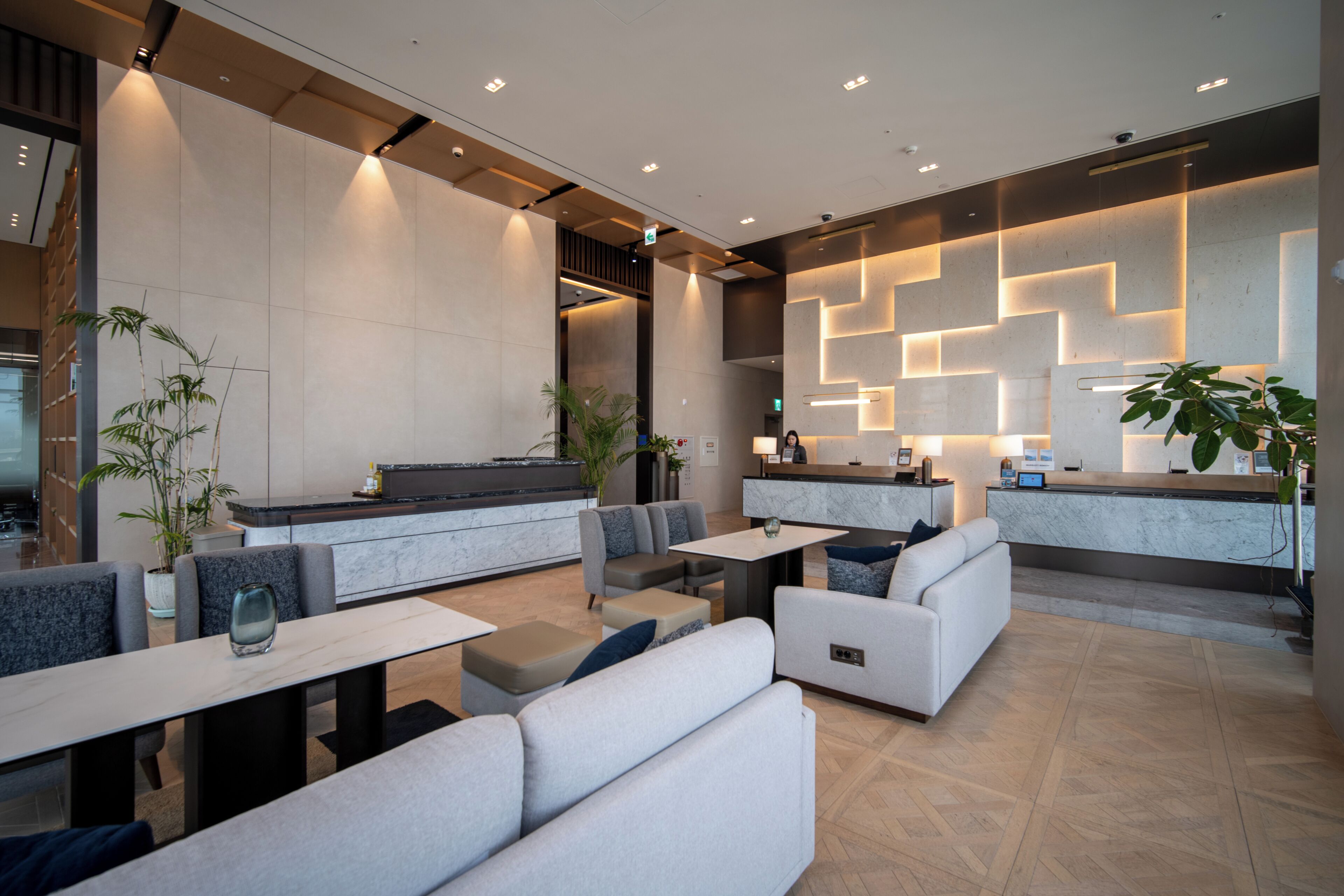 A modern lobby with seating areas, a reception desk, and a large potted plant.