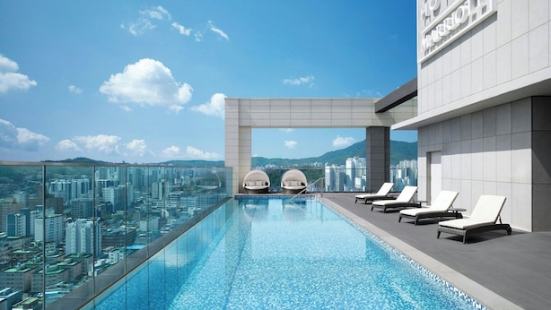 A rooftop infinity pool with lounge chairs and a view of the cityscape.