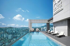 Una piscina infinita en la azotea con sillas de descanso y vistas a la ciudad.