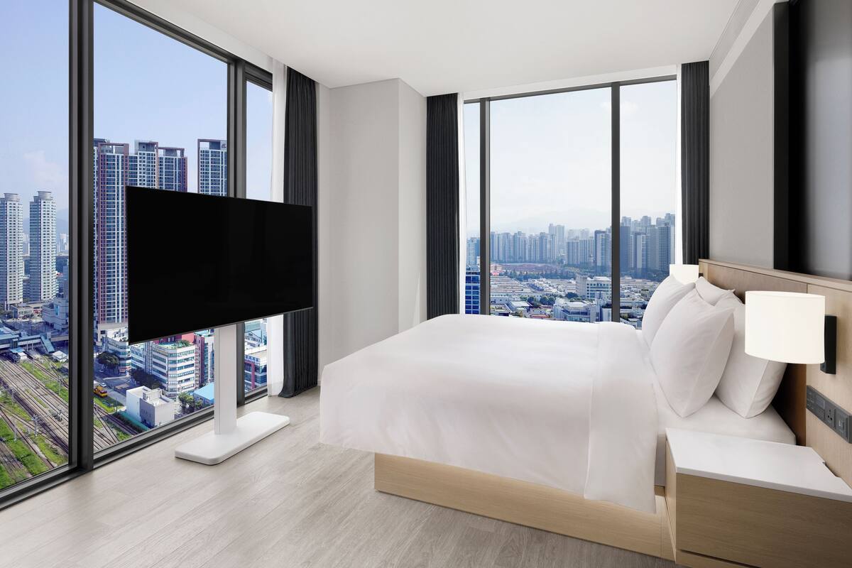 A modern hotel room with a large bed, a flat-screen TV, and a city view.