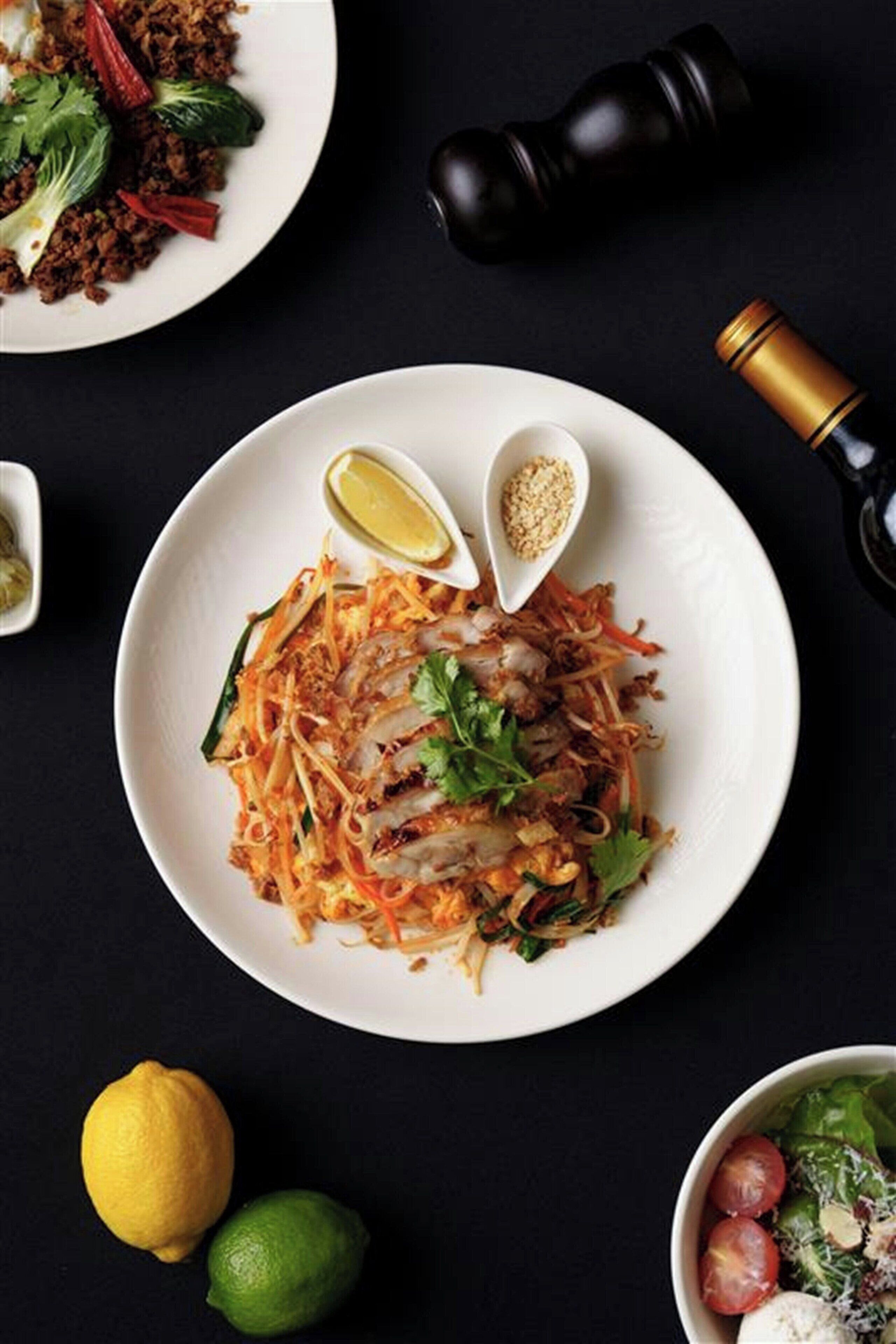 A plate of Pad Thai with lime wedges and peanuts on a dark background.