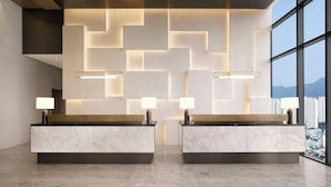 A modern reception desk with a geometric light pattern on the wall, two lamps, and a city view through large windows.