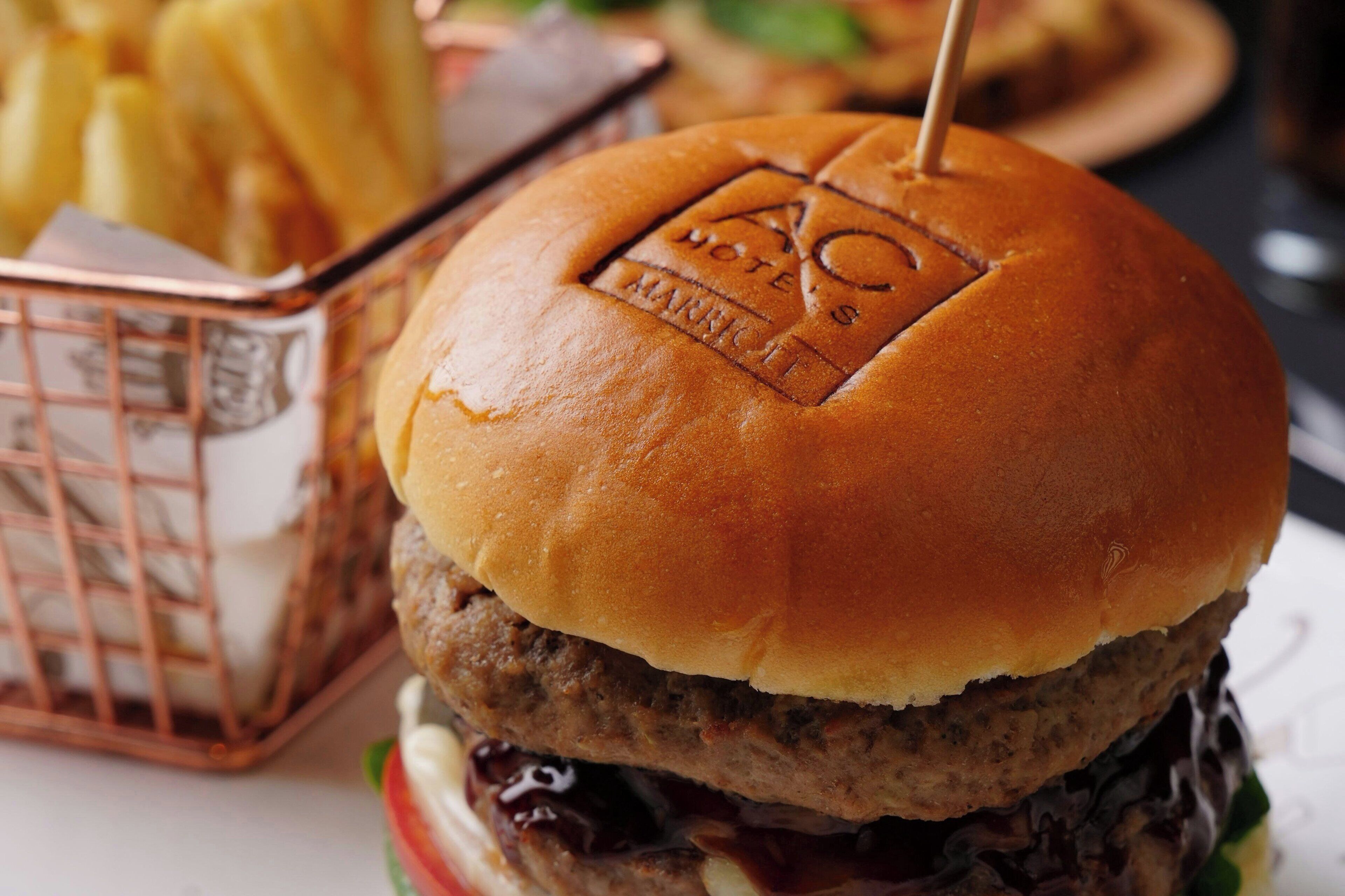 Una hamburguesa con un pan tostado, una porción de papas fritas y una cesta de papas.
