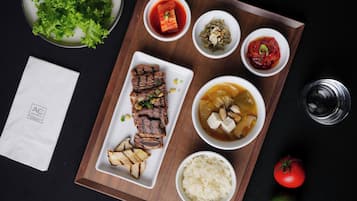 A tray with grilled meat, rice, and various side dishes, including kimchi and a soup with tofu.