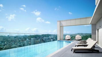 Relax by the rooftop infinity pool overlooking the cityscape, surrounded by lounge chairs and unique seating pods.