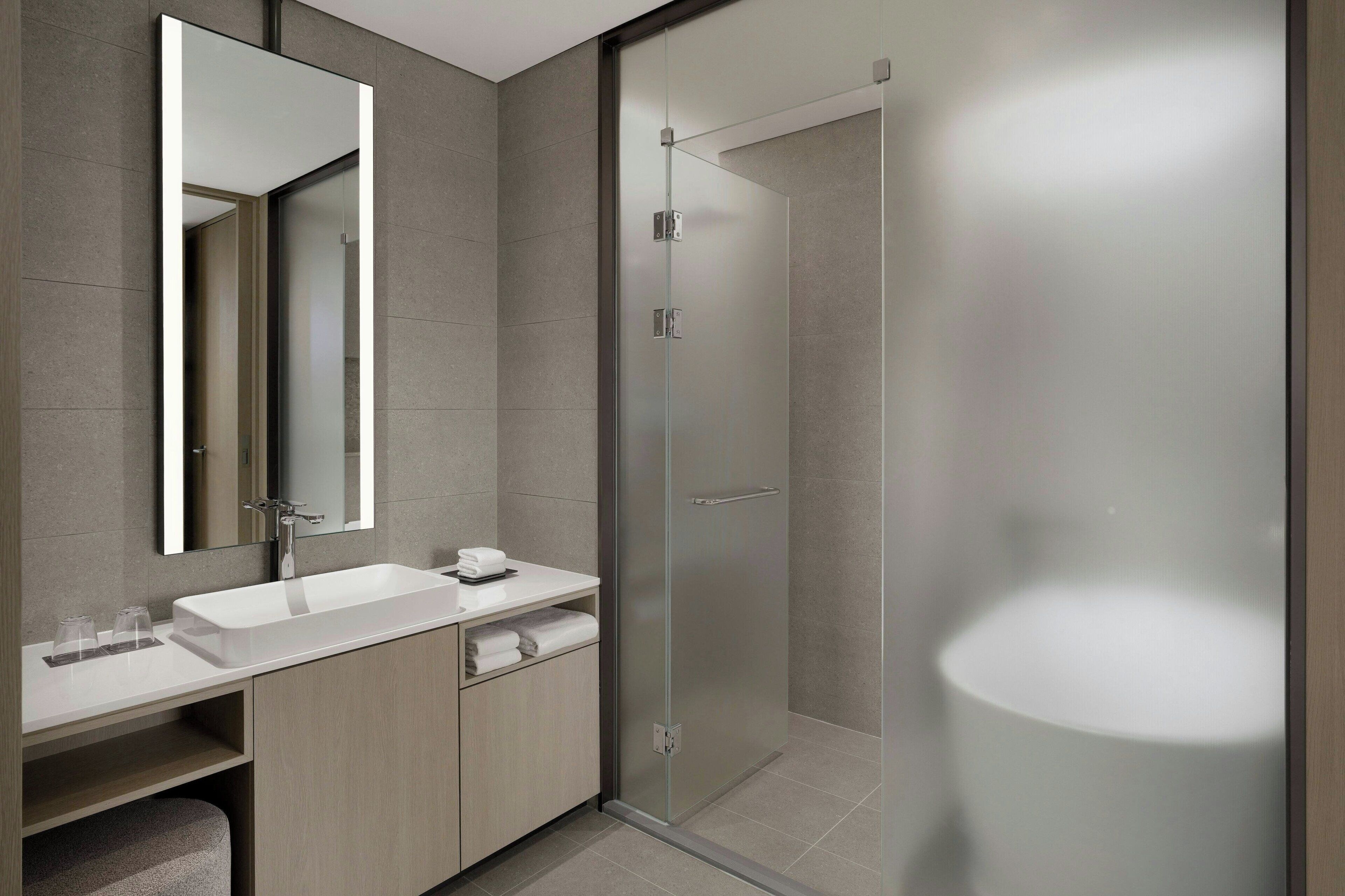 Un baño moderno con un espejo grande, un lavabo blanco y una cabina de ducha de vidrio.