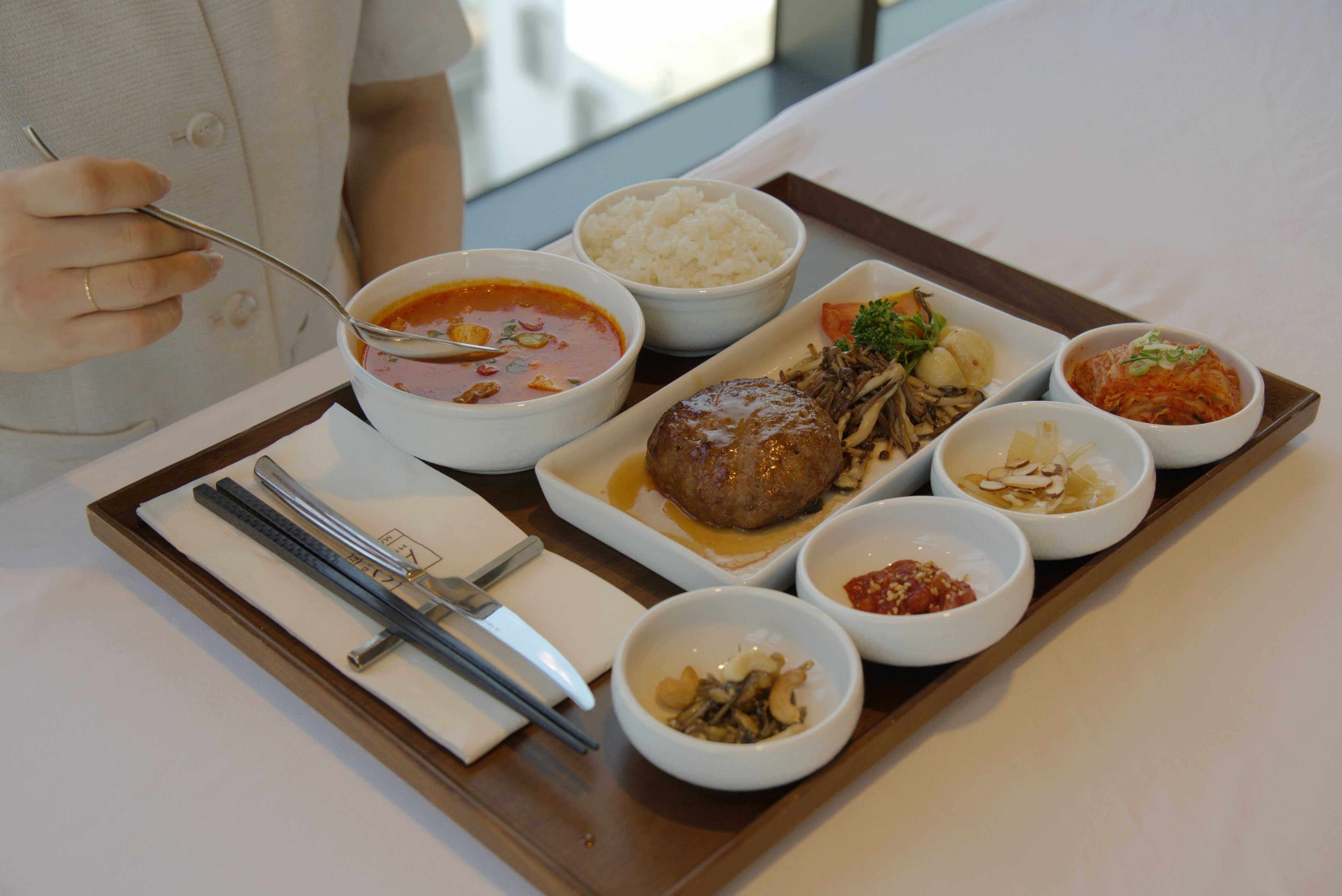 A tray with various dishes including rice, soup, and meat, accompanied by chopsticks and a spoon.