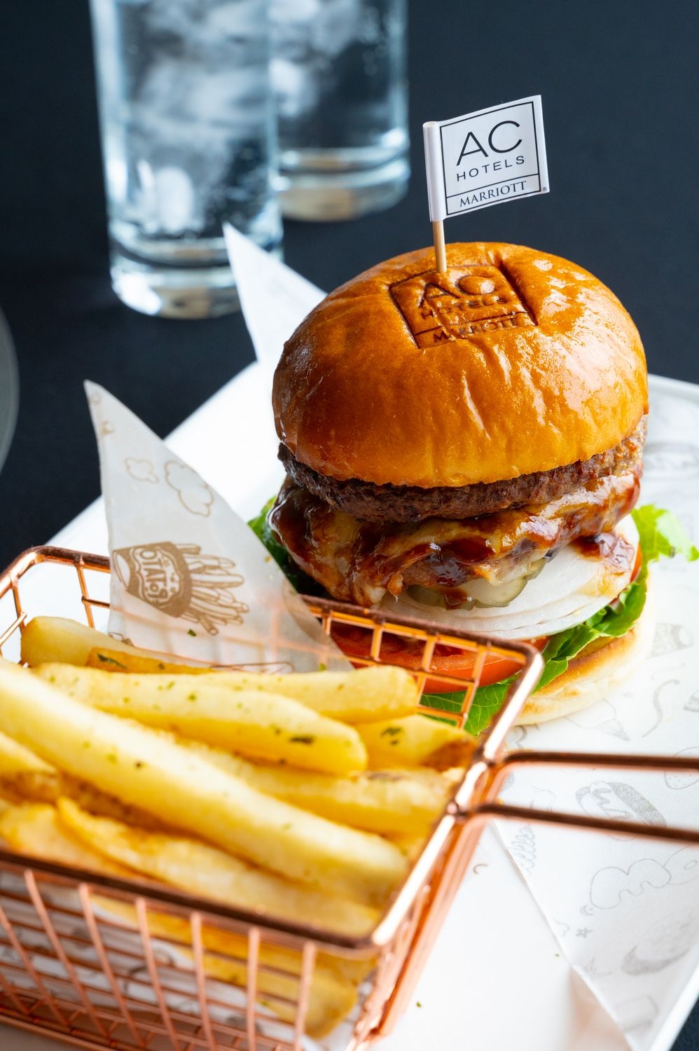 A burger with a flag on the bun, accompanied by a basket of fries.