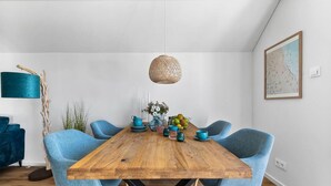 Ein Essbereich mit Holztisch, blau gepolsterten Stühlen, einer gewebten Pendelleuchte und einem gerahmten Kunstwerk an der Wand.