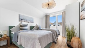 Ein modernes Schlafzimmer mit zwei Betten, einem großen Fenster mit Aussicht und einer hängenden Leuchte.